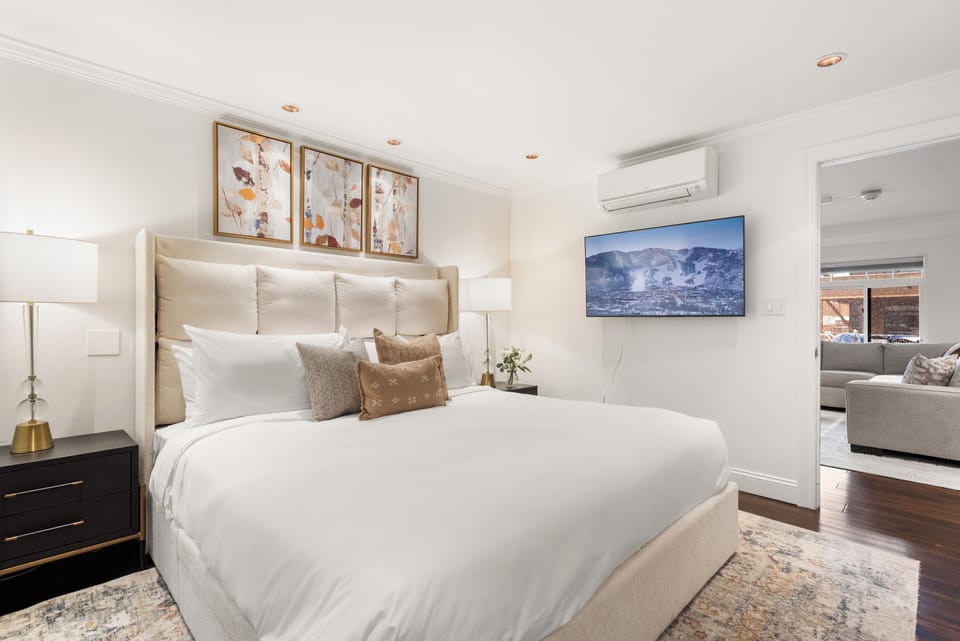 Spacious primary bedroom with TV, king-sized bed, luxury linens, plush mattress, and ensuite bathroom.