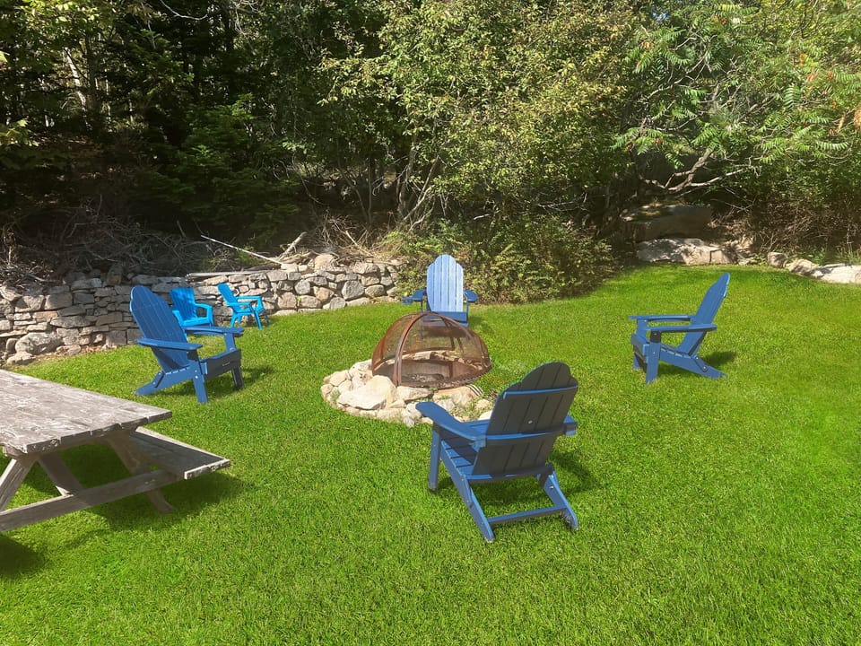 The expansive main lawn features a stone fire pit with Adirondack chairs, ideal for stargazing on the "Quiet Side." Adjacent to a private picnic table, this pet-friendly outdoor space offers plenty of room for family gatherings and relaxing after a day.
