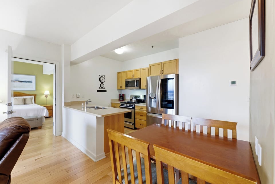 Kitchen and Dining Area:
Bright kitchen and dining space with wood cabinetry, stainless steel appliances, breakfast bar, and natural wood dining table.