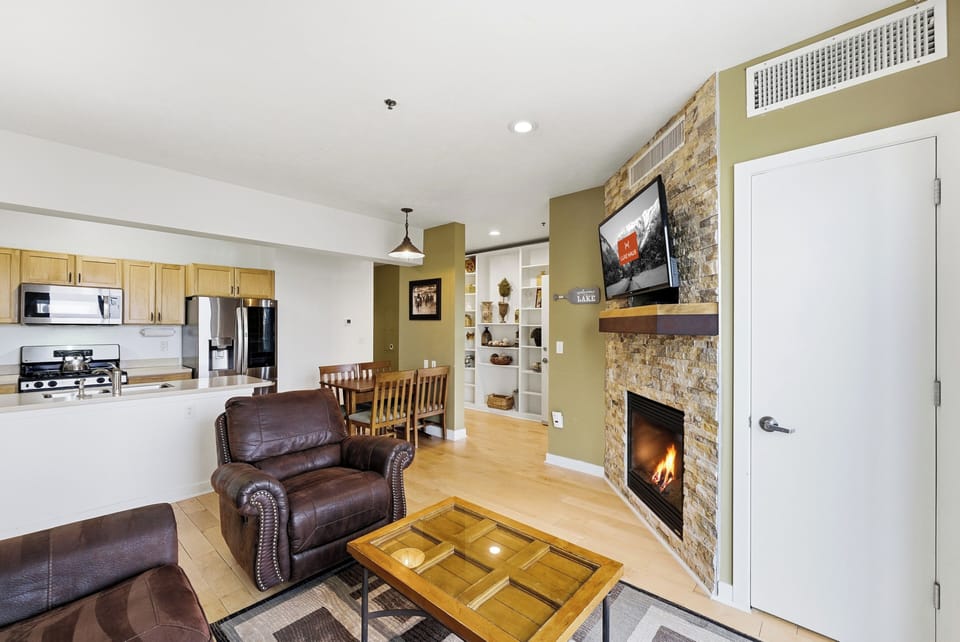Living Area with Fireplace and Bedroom View:
Open living space featuring stone fireplace, leather armchair, wood coffee table, and view into primary bedroom.