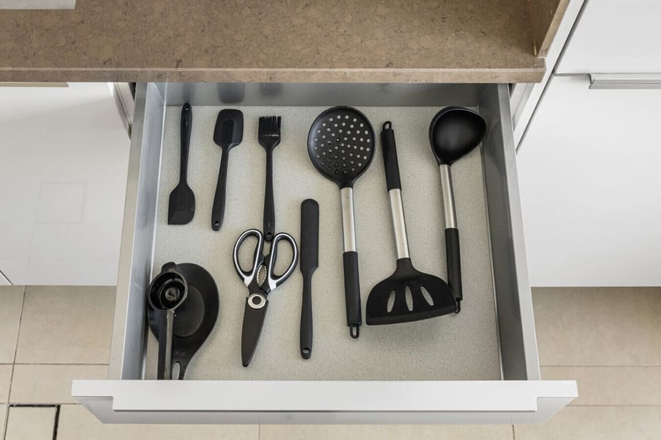 Organized drawer with cutlery, measuring spoons, and kitchen essentials.