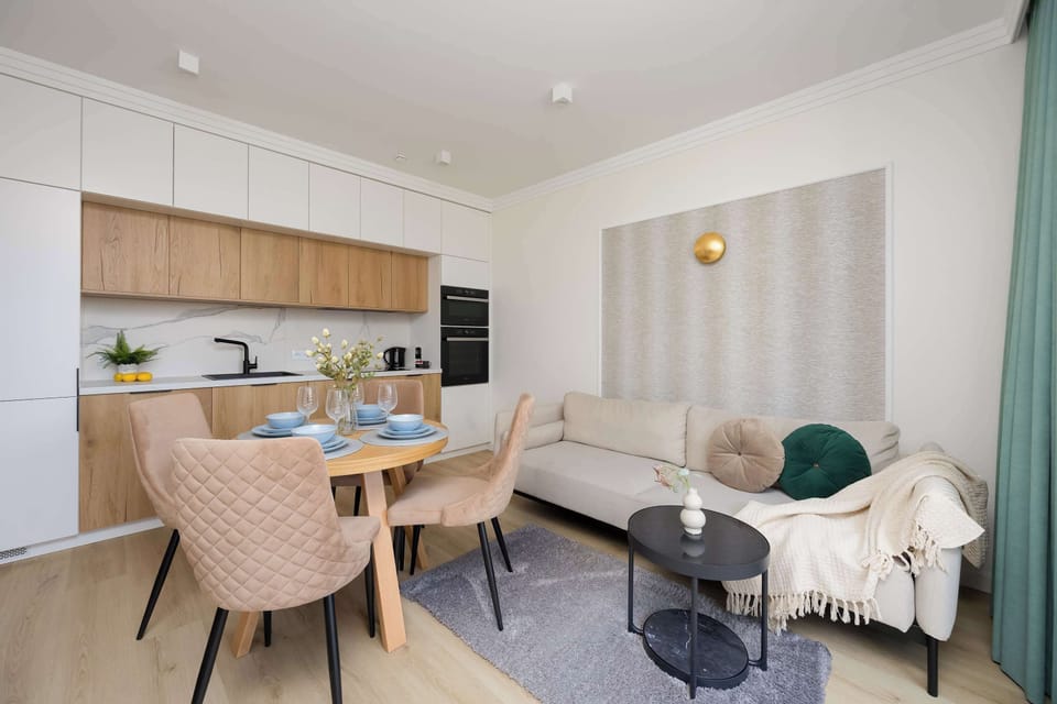 The open-concept area connects a modern kitchenette with wooden cabinetry to a dining set and a cozy lounge corner.