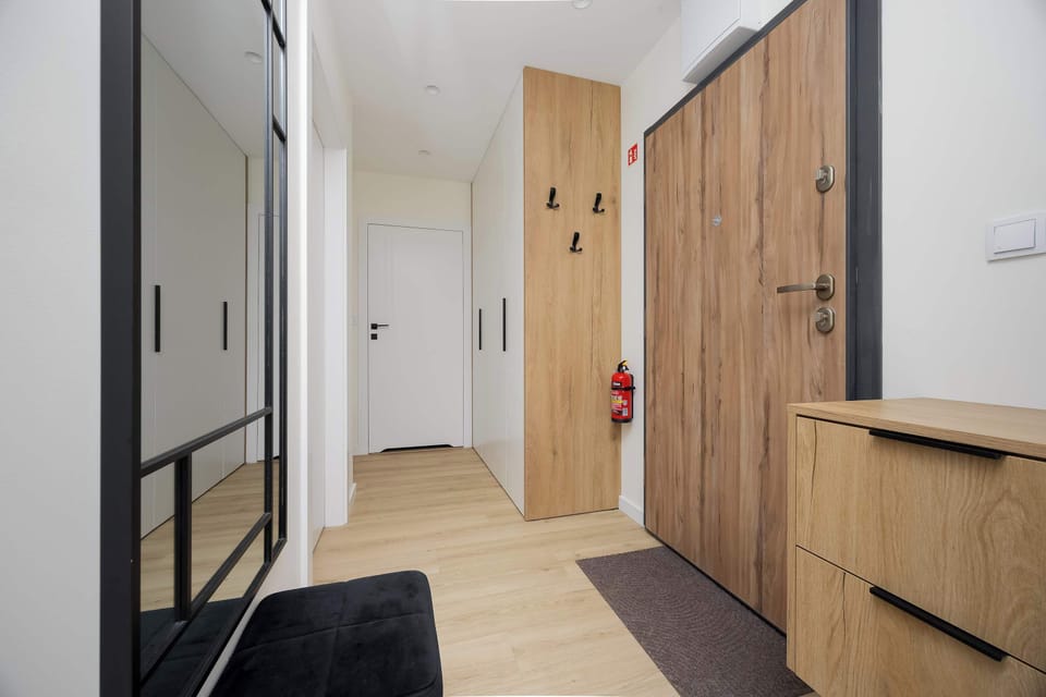 The entrance area is bright and welcoming, featuring light wood flooring, a large mirror, and functional storage cabinets.