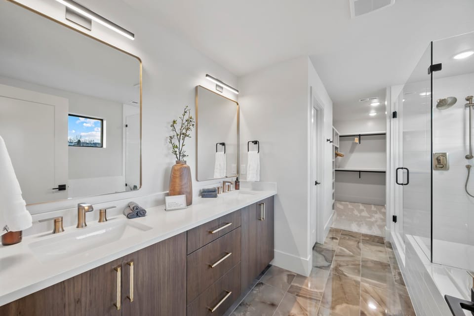 A large dual vanity bathroom with separate soaking tub and large glass shower enclosure and spacious walk in closet