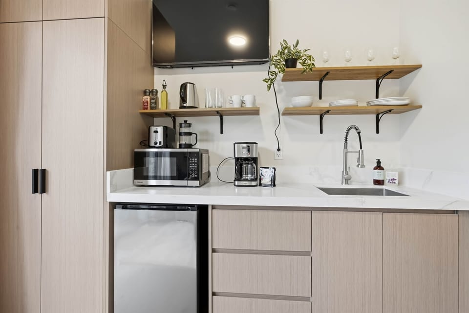 Kitchenette with microwave, toaster, coffee machine, kettle, sink, mini fridge and tv above the kitchen.