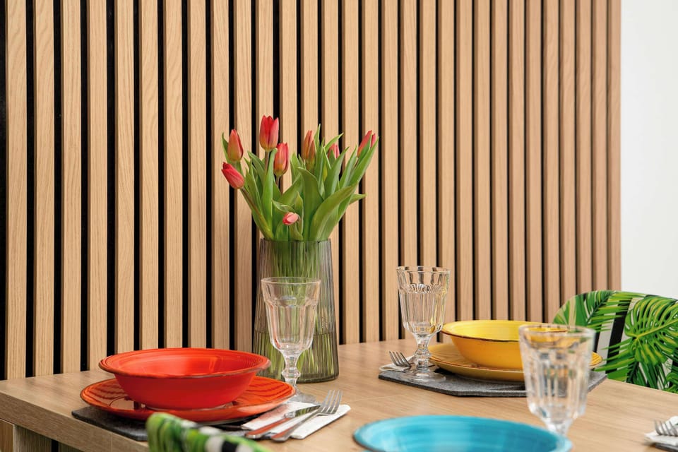 A close-up of the dining table shows a vibrant arrangement of red tulips in a glass vase alongside colorful tableware. This decorative touch adds a pop of color to the modern, wood-accented interior.