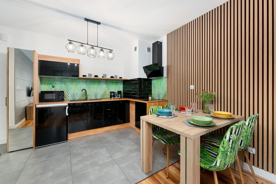 The dining area is marked by a wooden table paired with unique green patterned chairs, set against a wall of vertical wooden slats. The open-plan layout connects the dining space directly to the modern kitchen.
