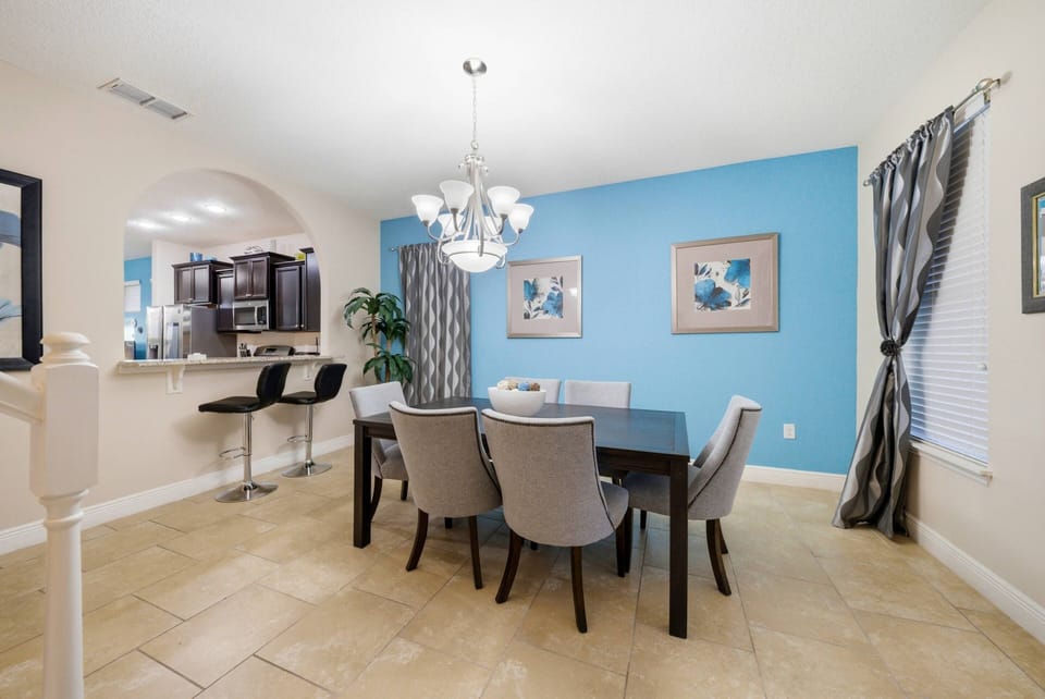 This bright dining area features a sleek black table and plush gray chairs, perfect for gatherings. A vibrant blue accent wall and elegant lighting create an inviting ambiance for you and your loved ones to enjoy together.