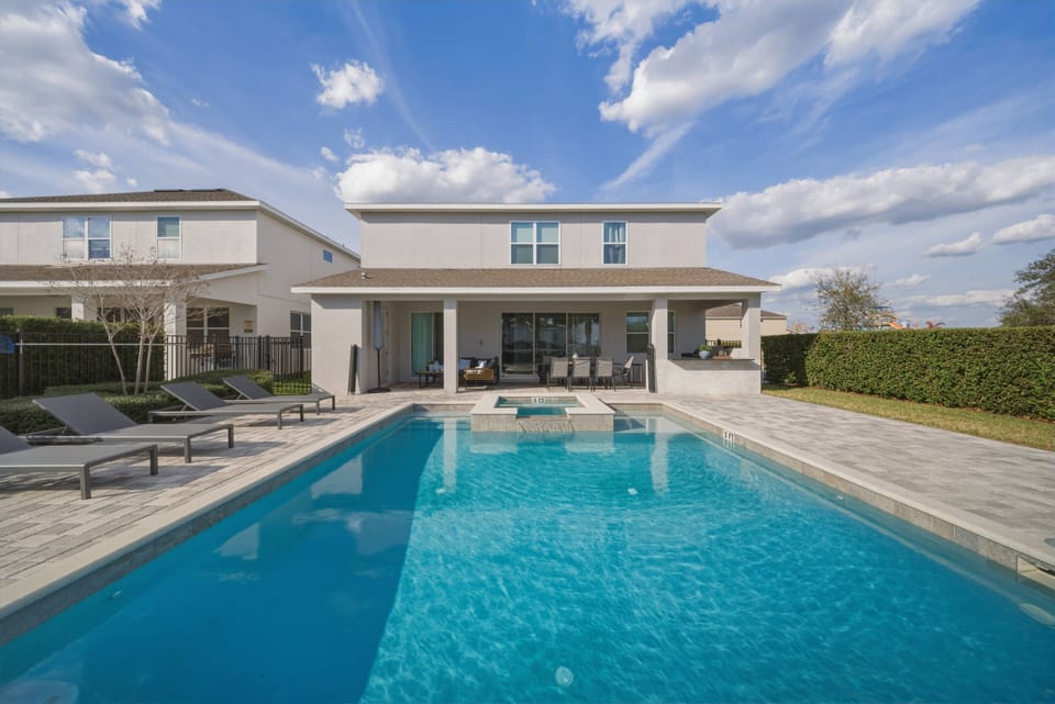 Step outside to a beautiful pool area with chic lounge chairs and lush hedges, perfect for sunbathing. The spacious patio seamlessly connects indoor comfort to outdoor leisure, inviting you to unwind under the beautiful skies.