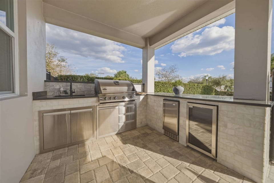 Step into this stunning outdoor kitchen, where sleek stainless steel appliances complement the warm stone flooring. Natural light floods the space, enhancing the inviting atmosphere while you prepare meals amidst beautiful views.