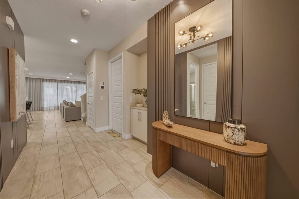 Enter a stylish entryway with warm tones and clean lines, featuring a sleek wooden console and a chic mirror. Soft lighting beautifully highlights the elegant tiled floor, inviting you to explore the home further.