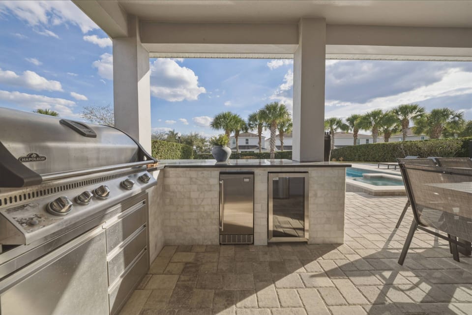 Enjoy outdoor dining at its finest with a sleek stainless steel grill and a chic bar area surrounded by palm trees. The cool stone tiles and open layout create the perfect setting for sunny days and warm evenings.