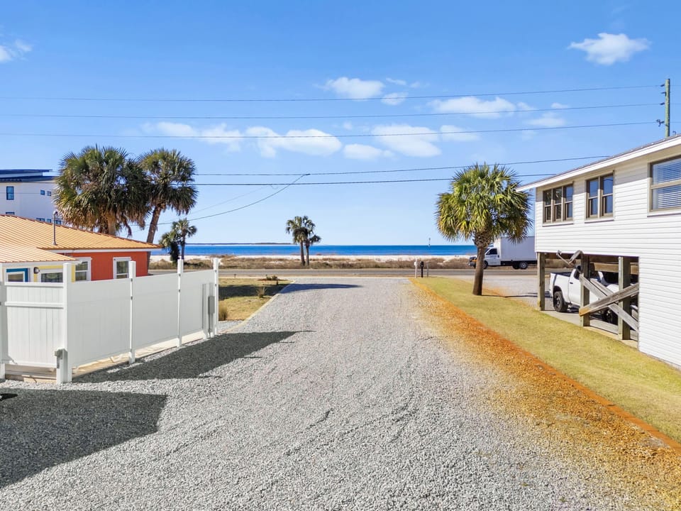 Coastal neighborhood with palm-lined street leading toward the beach, featuring colorful vacation homes and ocean views.