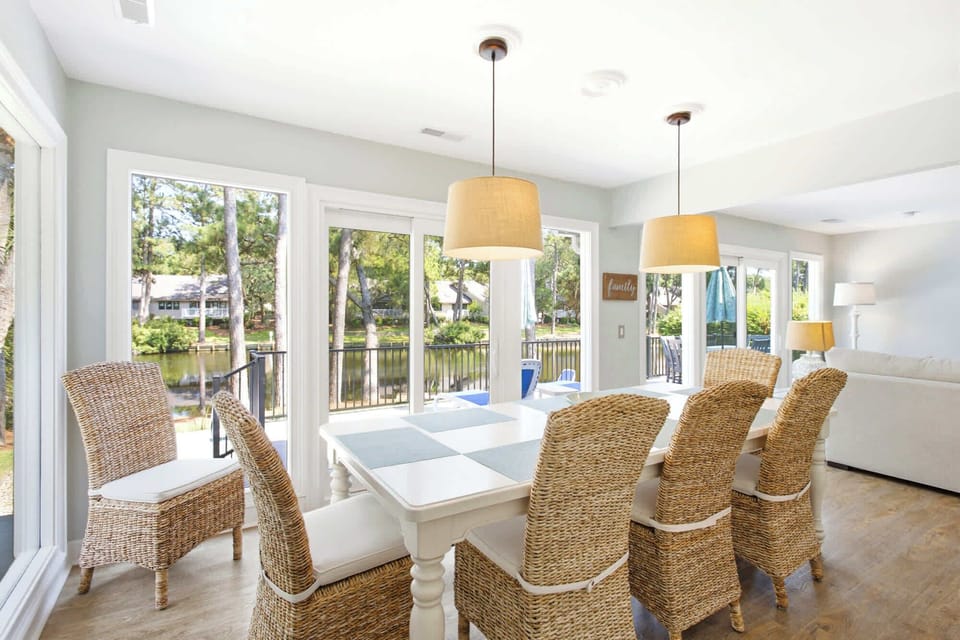 Dining area with woven chairs and large windows overlooking a peaceful lake view