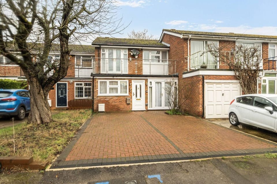 Front exterior of a brick house with a block-paved driveway, a white front door, and an integral garage with a white up-and-over door.