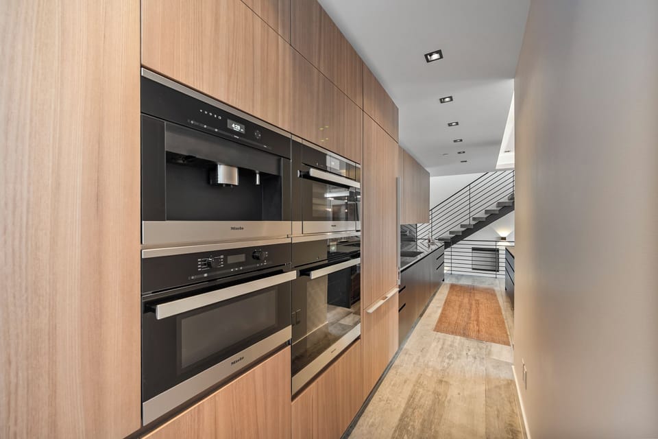 Your sleek modern kitchen features premium appliances and warm wood cabinetry, perfect for preparing meals in sophisticated style.