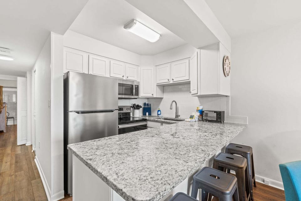 Bright kitchen with granite countertops, stainless steel appliances, and bar seating - ideal for meals and gathering.