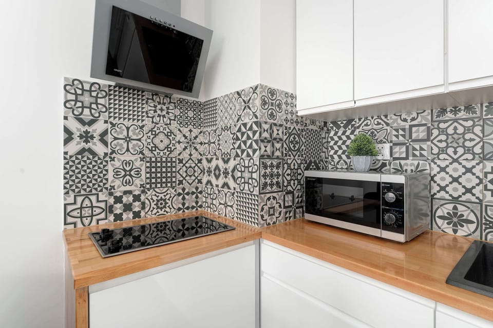 A close-up of the kitchen corner highlighting the stovetop and microwave. The geometric patterned tiles stand out as a strong visual element. Wooden countertops add warmth to the white cabinetry.