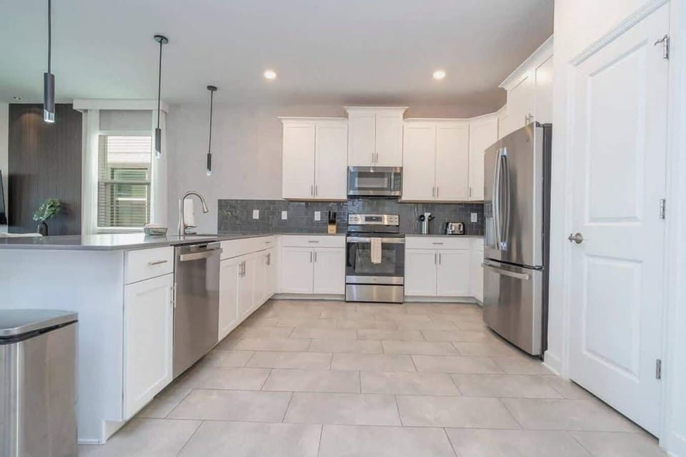 Modern, sleek white kitchen with stainless steel appliances, ample counter space, and stylish gray tile backsplash for a contemporary look.