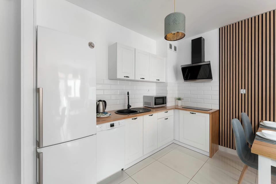 The kitchenette is equipped with white cabinetry, a large fridge, and a dark backsplash. Wooden slats on the wall create a stylish transition between the cooking and dining areas.