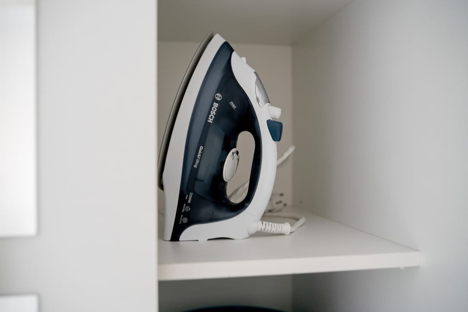 A domestic iron is stored neatly on a white shelf, ready for use. This detail highlights the apartment's readiness for longer stays or business trips.