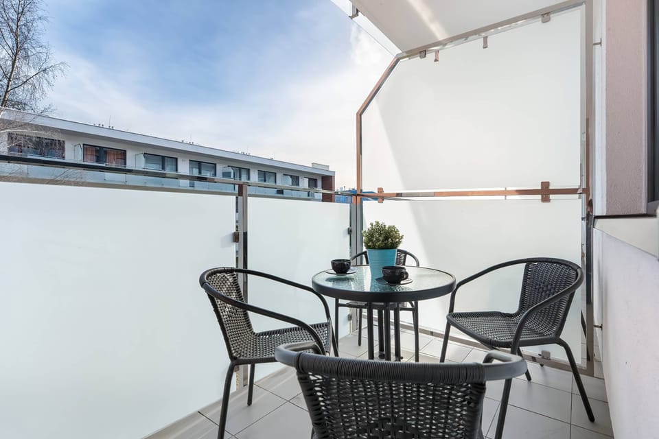 A small round table with two chairs sits on the balcony, offering a private spot for morning coffee. The space is clean and modern, extending the living area outdoors.