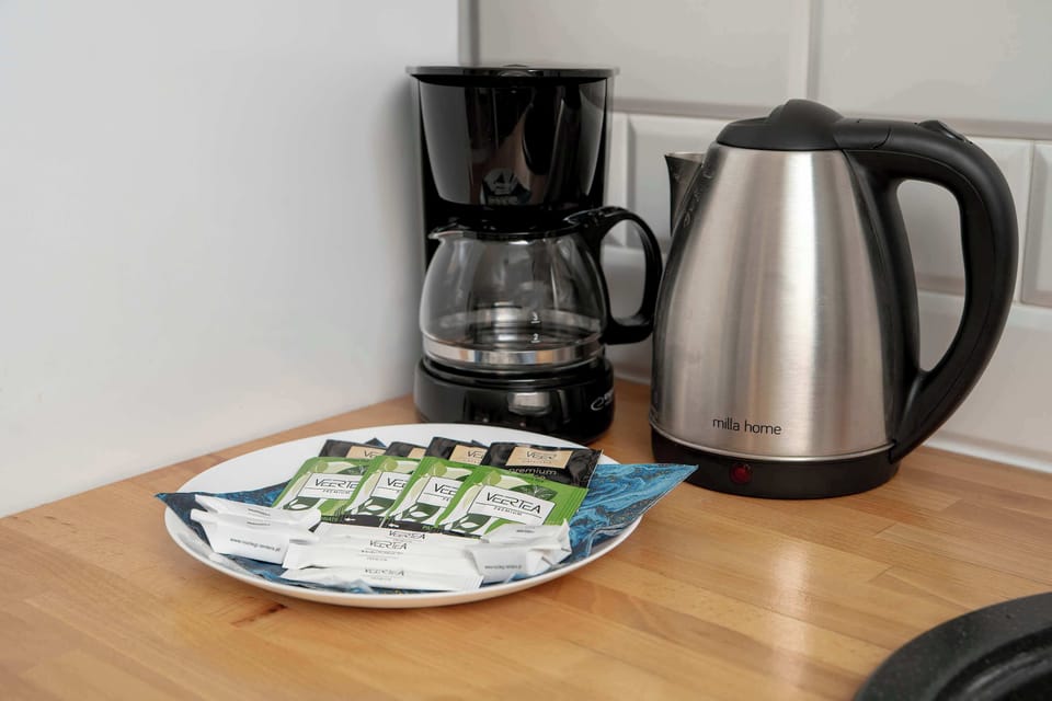 A countertop detail shows a drip coffee maker and an electric kettle ready for use. A small plate with tea bags and sugar is prepared for the guests' arrival.