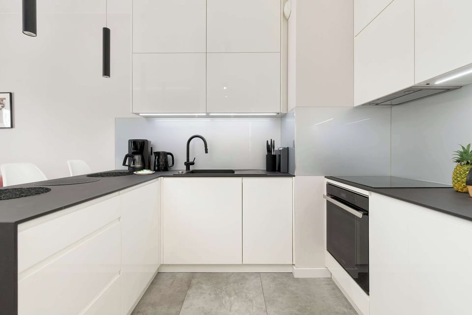 Close-up perspective of the kitchen reveals a clean, handle-less design and integrated oven under the induction hob. Subtle under-cabinet LED lighting provides both functionality and a warm ambiance.