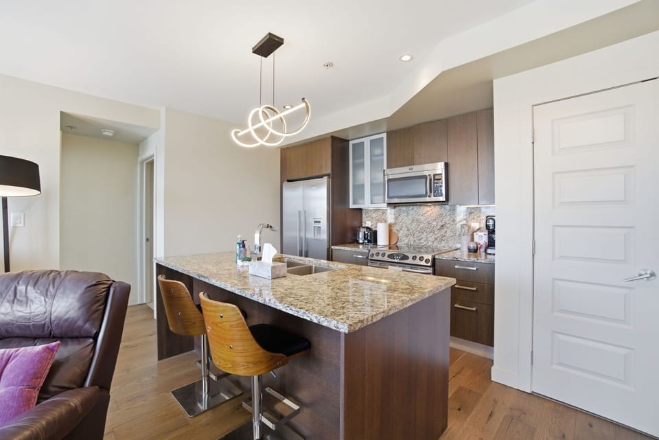 Modern kitchen with granite island, stainless steel appliances, bar seating, and stylish lighting—perfect for cooking and entertaining.
