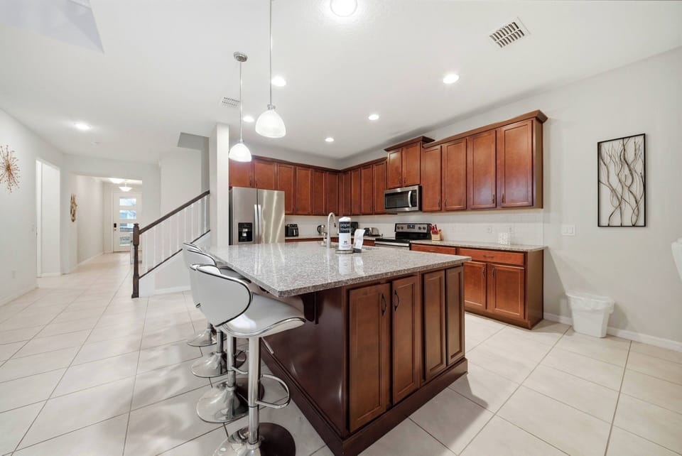 This stylish kitchen features rich wooden cabinetry that contrasts beautifully with the sleek granite countertops. The modern bar stools invite casual dining, while overhead lighting adds a warm glow to the inviting atmosphere.