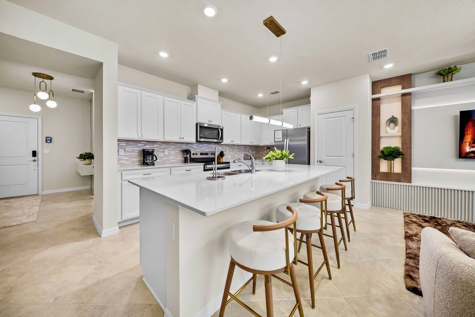 Welcome to this stylish kitchen with a spacious white island and inviting bar stools for casual gatherings. The modern appliances and sleek cabinetry create a bright, functional space, enhanced by cozy decorative accents.
