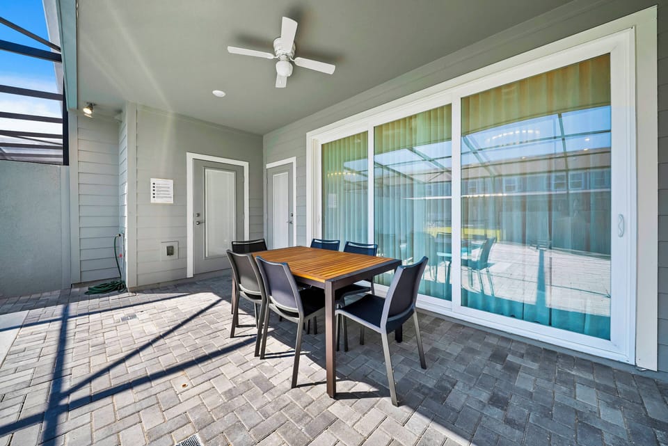 Step outside to a stylish dining area with a sleek wooden table and modern chairs, perfect for enjoying meals al fresco. Expansive sliding doors fill the space with natural light, enhancing its tranquil and inviting atmosphere.
