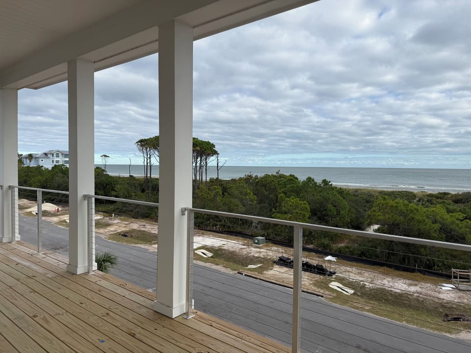 Expansive covered deck with ocean views overlooking coastal forest and sandy shoreline beneath dramatic cloudy skies.