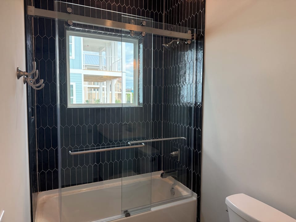 Step into your modern bathroom featuring elegant black geometric tiles and a glass-enclosed tub-shower combo with city views.