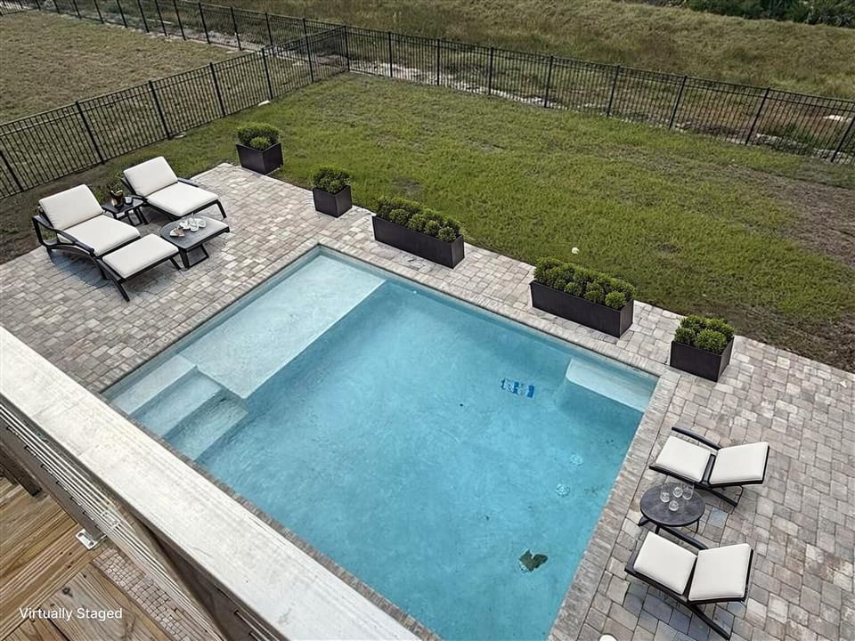Aerial view of the private pool area with lounge seating, decorative planters, and spacious paved deck surrounded by fenced yard.