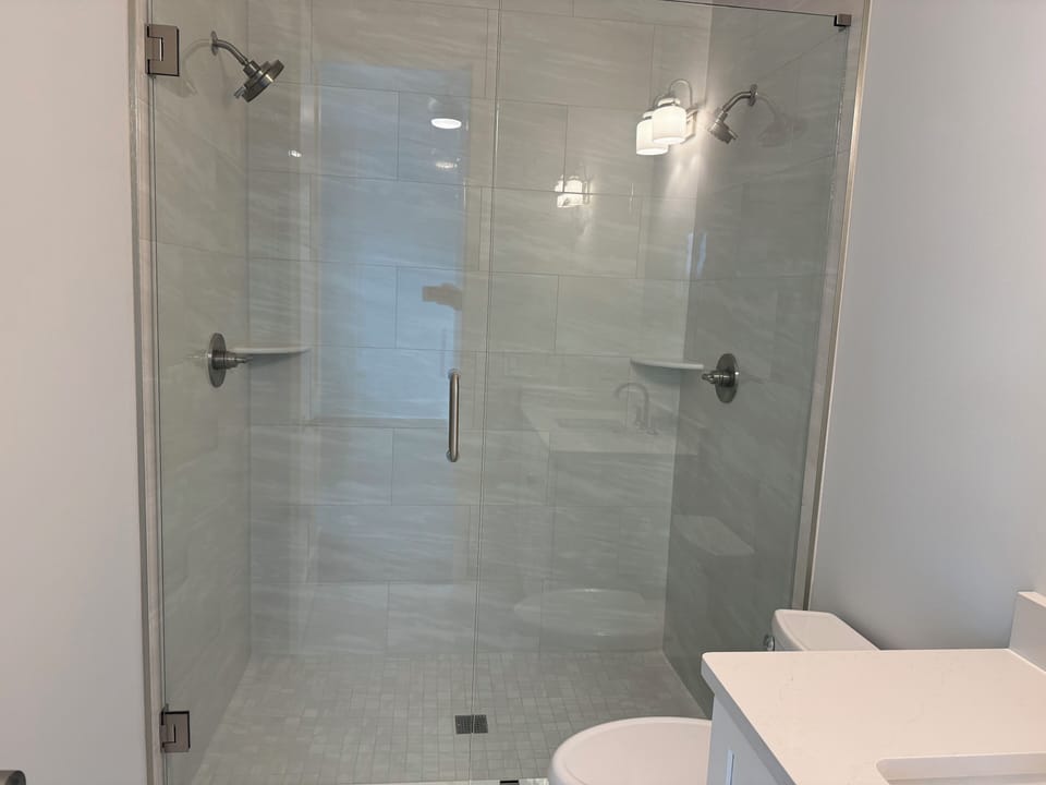 Step into your luxurious glass-enclosed shower with dual rainfall heads and built-in seating for the ultimate spa experience.