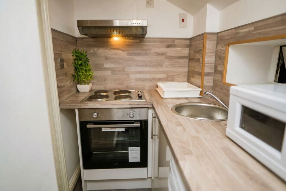 Compact kitchen with wood-effect tiles, oven, hob, and microwave all ready to use.