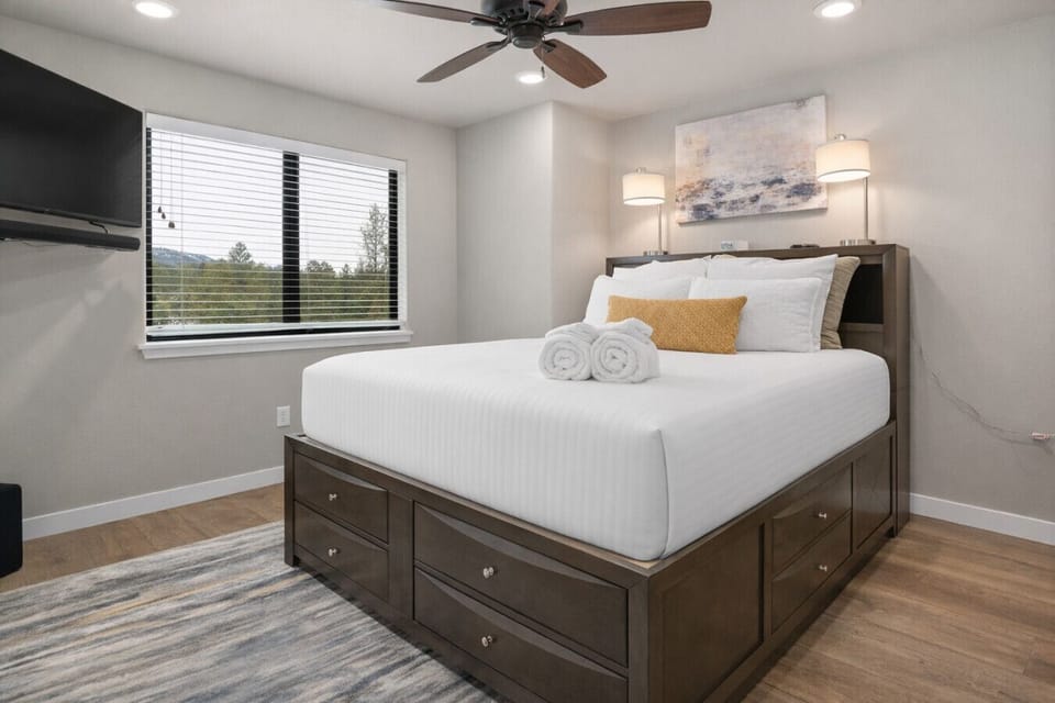 A spacious bedroom with crisp white linens, ceiling fan, and large windows offers both comfort and natural light.