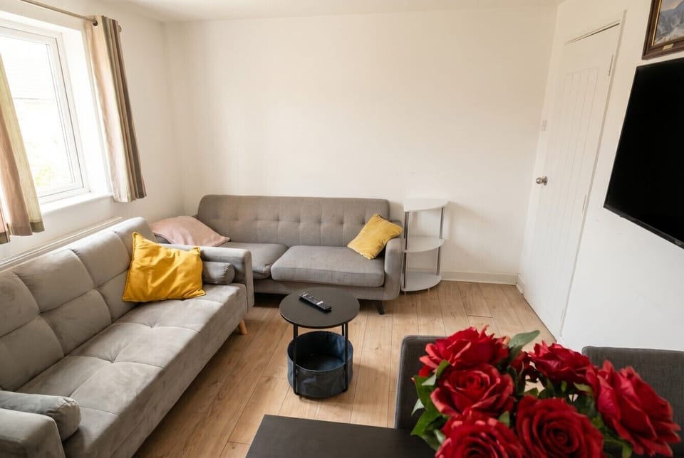 Bright lounge with two sofas, wall-mounted TV, and fresh roses to welcome you.