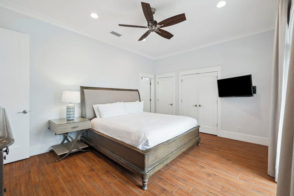 Unwind in your spacious bedroom featuring a plush king bed, mounted TV, and gentle ceiling fan for ultimate comfort.