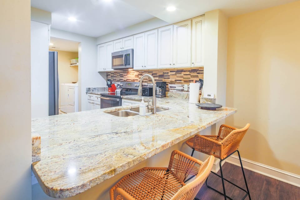 Sea Glass features a renovated kitchen with white cabinets, tiled backsplash and granite counters.