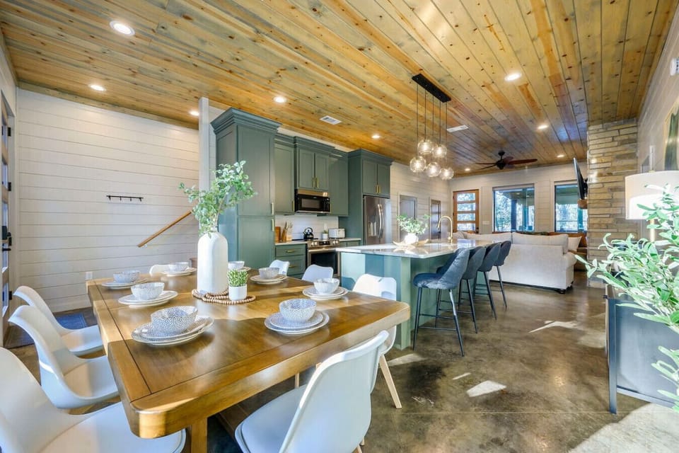 This open-concept kitchen and dining area features custom green cabinetry, a wood ceiling, and tons of natural light from the windows.