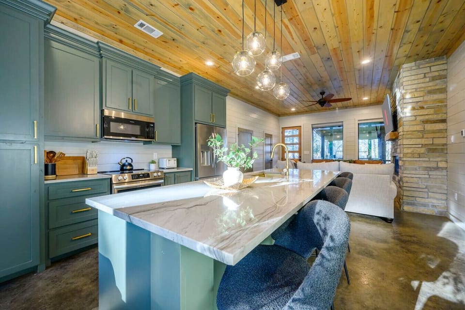 This modern kitchen features custom green cabinetry, marble countertops, and a gorgeous wood ceiling with pendant lighting.