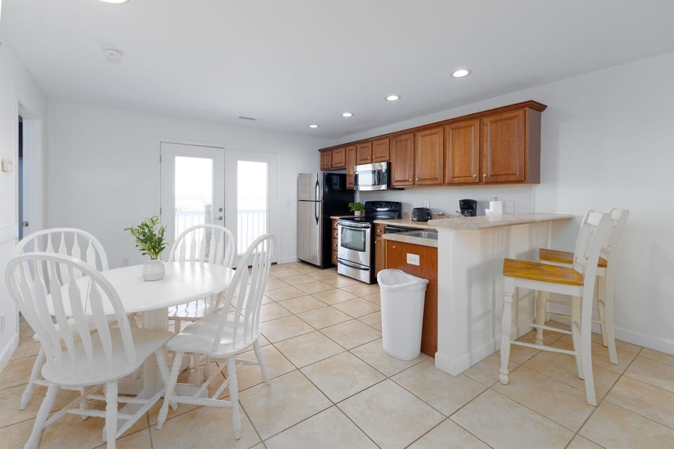Fully equipped kitchen with stainless appliances, breakfast bar seating, and a sunny dining area just steps from the balcony doors