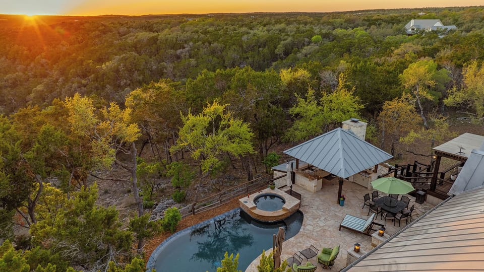 That golden hour glow over the Hill Country. Pool, hot tub, stone fireplace, dining area all of it wrapped in acres of cedar and oak trees as the Texas sky turns gold. This is what the end of a perfect day at Casa Colina looks like from above.