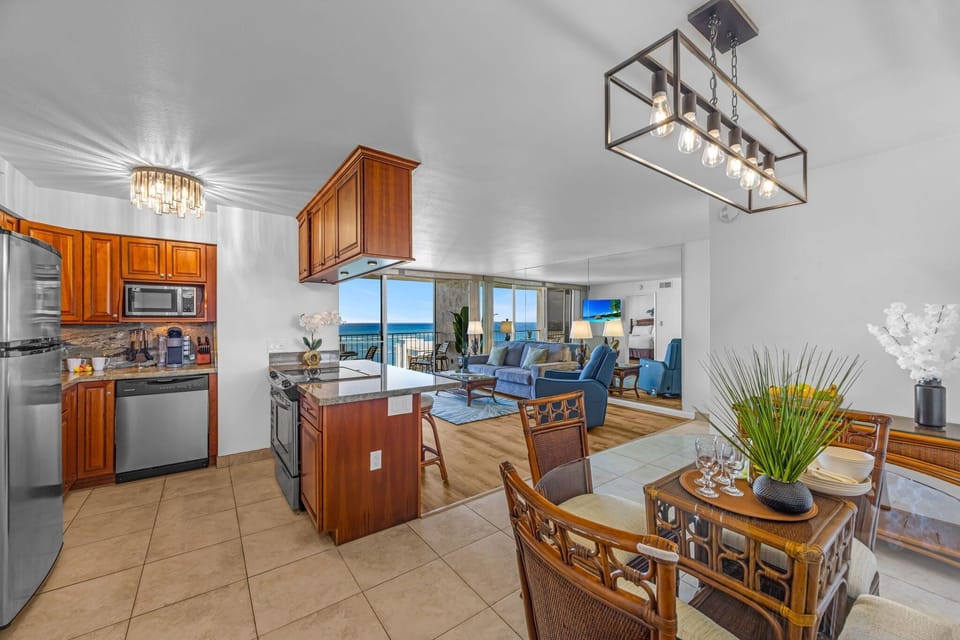 Open‑concept dining and kitchen area flowing into a bright living space with stunning ocean views just beyond the sliding door