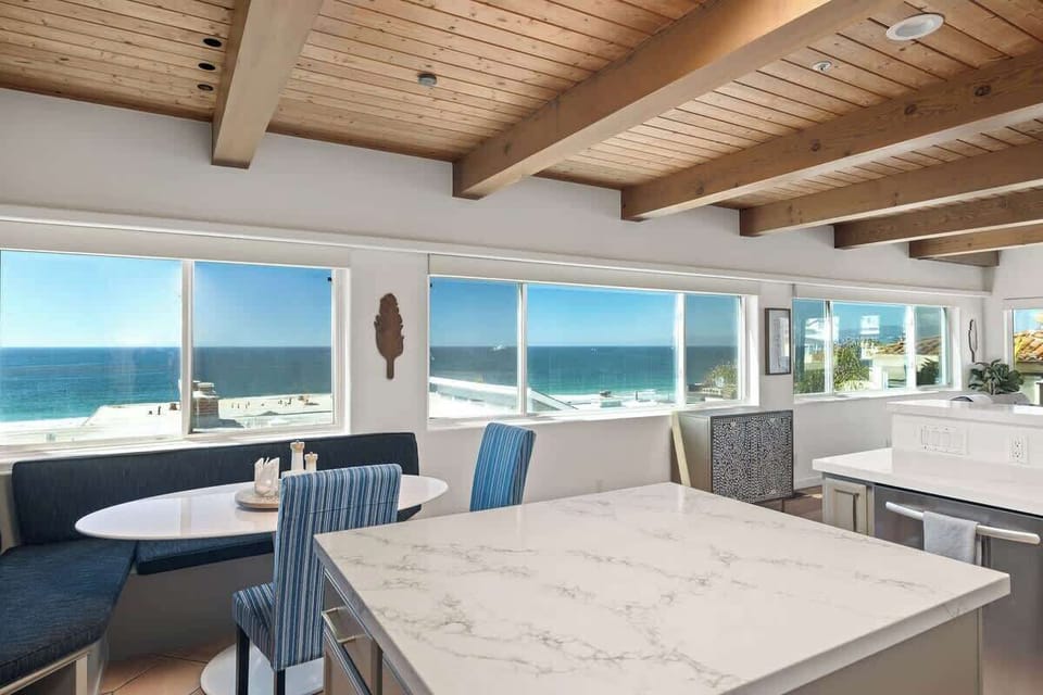 Bright kitchen and dining area surrounded by wide windows that bring in natural light and ocean views.