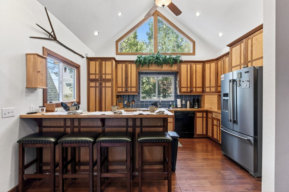 A bright, inviting kitchen with warm wood cabinetry, vaulted ceilings, and a spacious breakfast bar—perfect for morning coffee, shared meals, and easy entertaining.