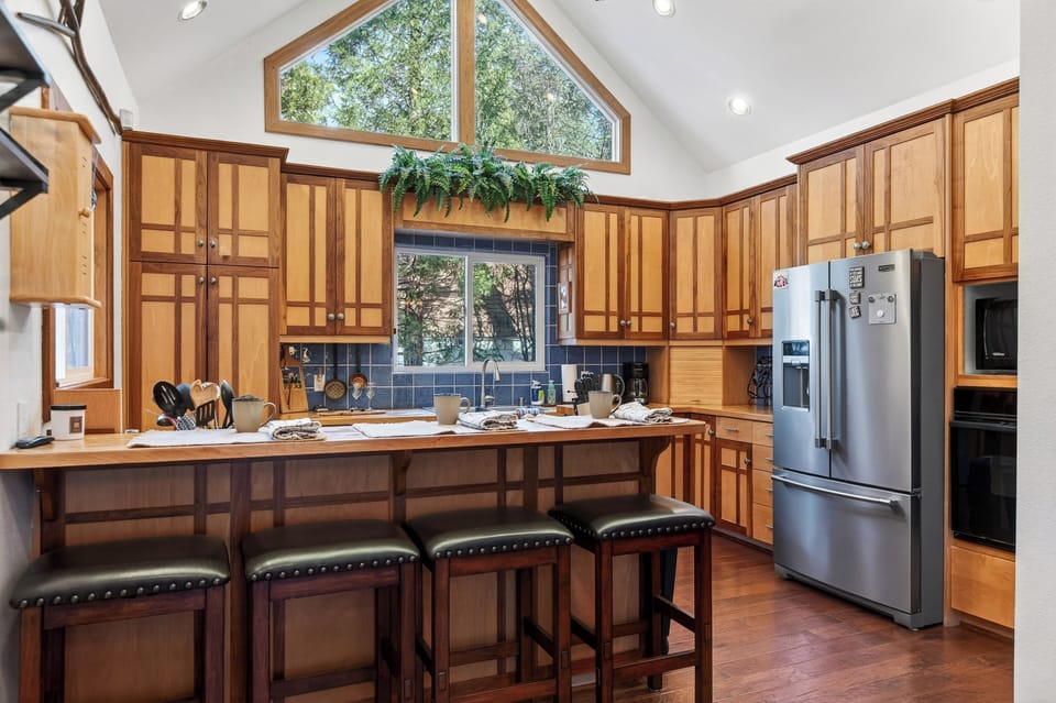 A bright, inviting kitchen with warm wood cabinetry, vaulted ceilings, and a spacious breakfast bar—perfect for morning coffee, shared meals, and easy entertaining.