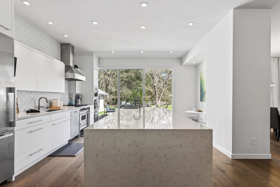 Sleek chef’s kitchen with a statement waterfall island and full wall of glass—bringing natural light and backyard views right to the heart of the home.